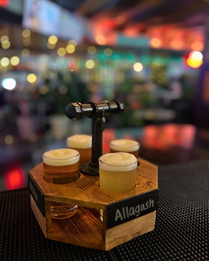A four-glass beer flight on a wooden tap-handle tray at the bar
