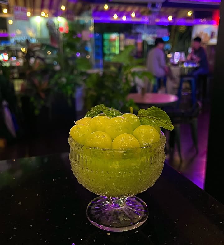 A frozen green melon drink with mint in a glass goblet, on the bar at night