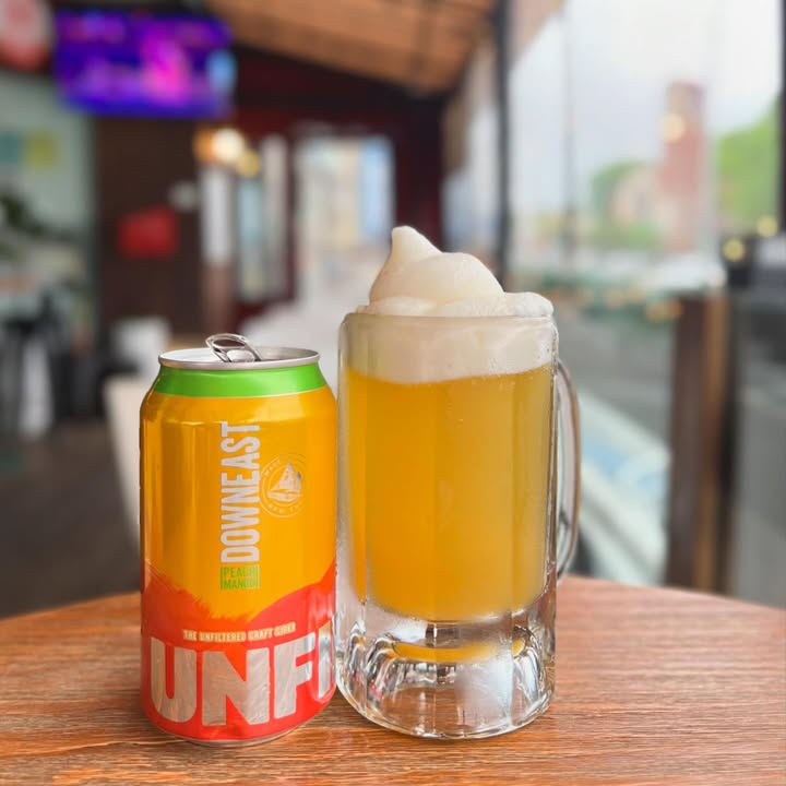 A cold can beside a foamy, frosted mug on a wooden table