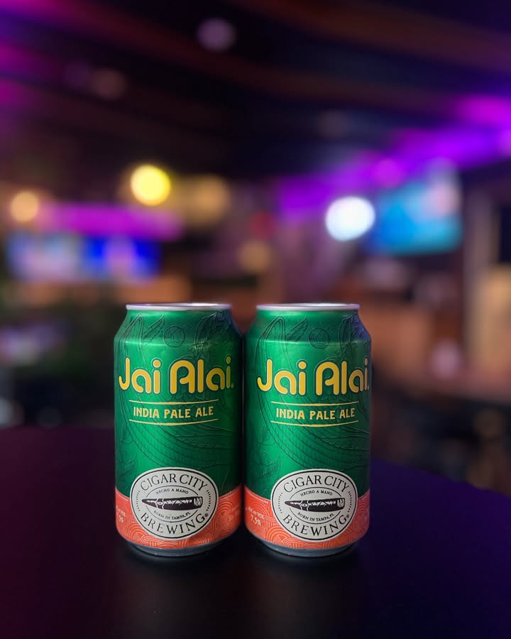 Two cans of Cigar City Jai Alai IPA under purple bar lights